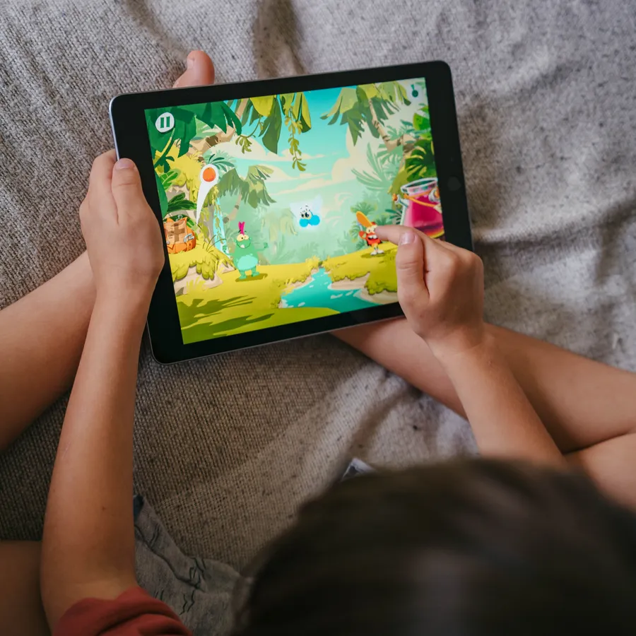 A child holding a tablet, playing a Poppins Learning reading game at home