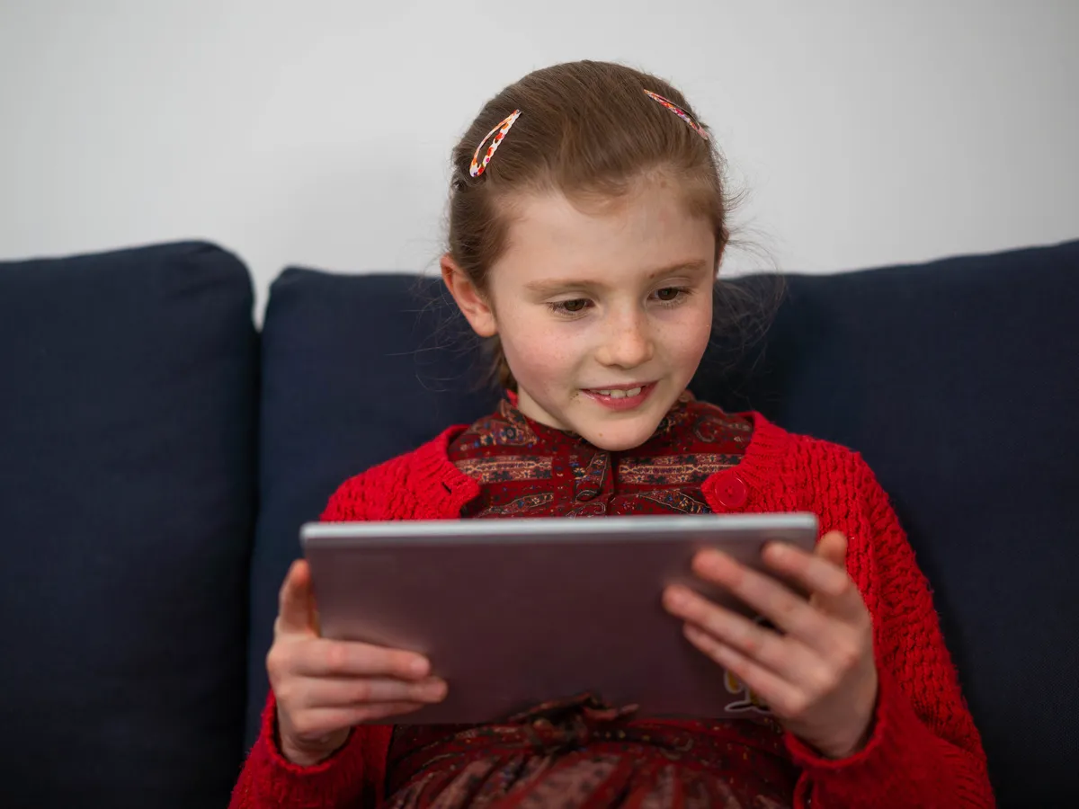 A child smiling while playing a reading game on a tablet at home